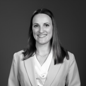 Portrait Mirjam Tercero in black and white - woman with long reddish-blonde hair and brown eyes in a suit with a necklace and a cheerful smile