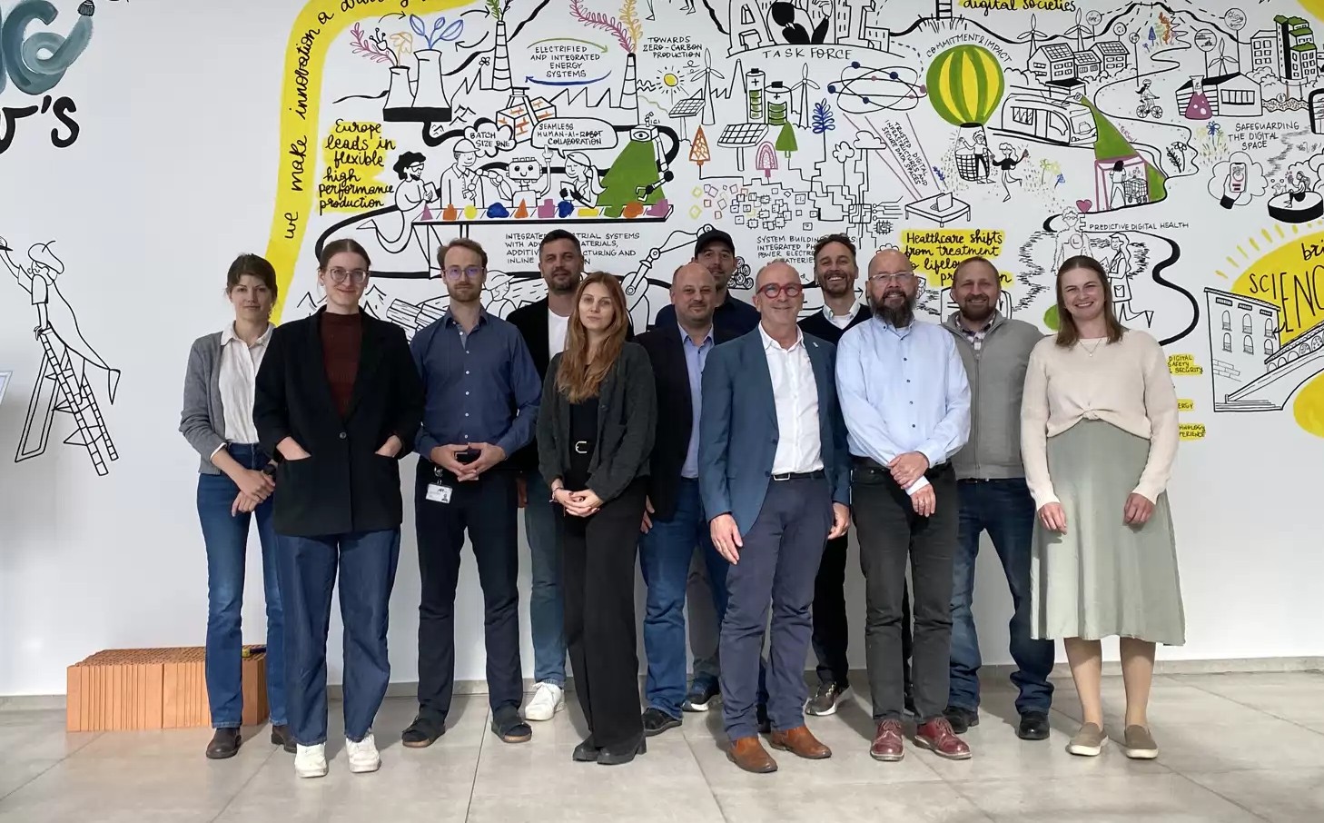 Gruppenfoto von zehn Teilnehmenden des VERITAS-Projektkonsortiums beim Kick-off-Workshop am Austrian Institute of Technology (AIT) in Wien am 20. Oktober 2026. Die Gruppe steht vor einer großflächig illustrierten Wand.